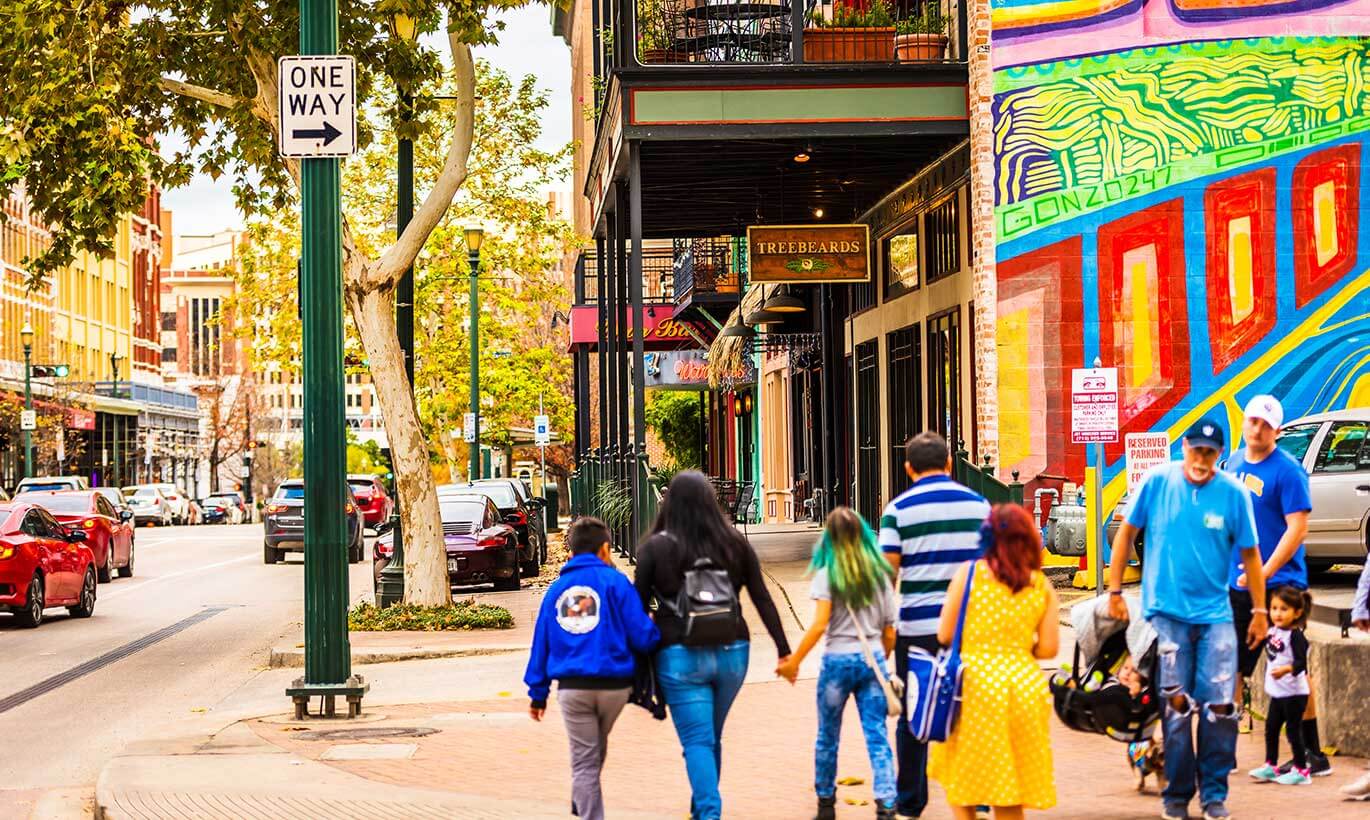 A family holds hands and walks next to a large colorful mural in downtown Houston, Texas.