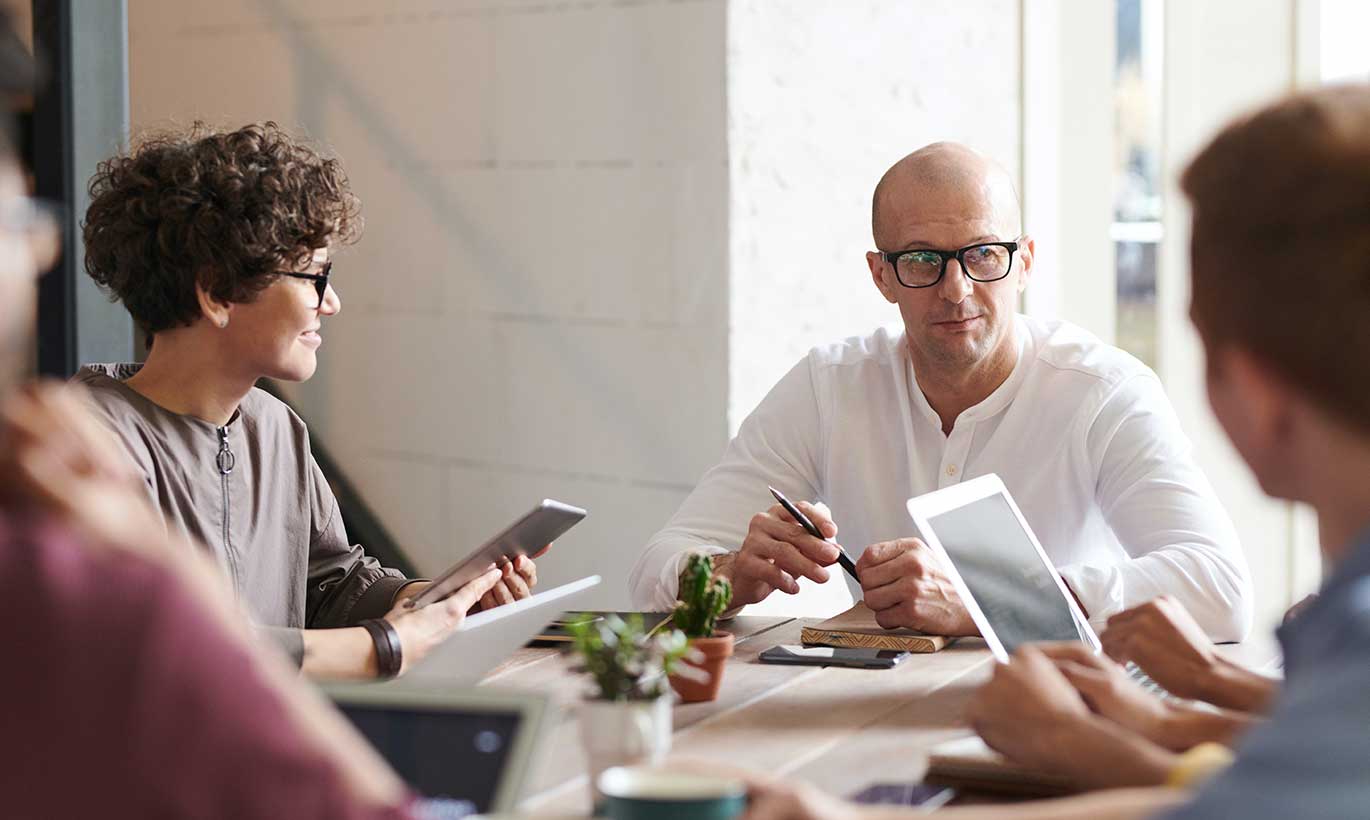 A man speaks to his three colleagues during a meeting while they all hold digital tablets