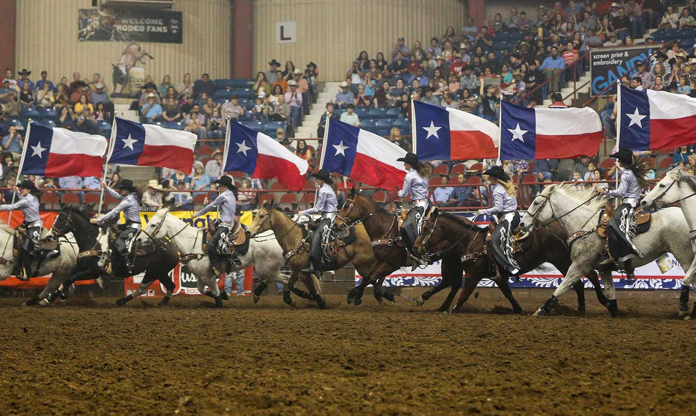 Cowgirls on horseback hold large Texas flags at the San Angelo Rodeo